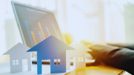 Modelos de casas de papel são colocados em uma mesa em frente a um laptop que exibe um gráfico de barras intitulado "Investimento imobiliário", ilustrando conceitos como Fundo de Investimento Imobiliário ou Aluguel.