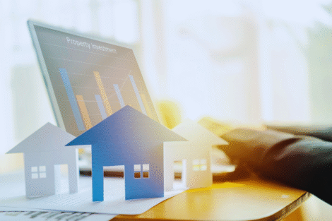 Modelos de casas de papel são colocados em uma mesa em frente a um laptop que exibe um gráfico de barras intitulado "Investimento imobiliário", ilustrando conceitos como Fundo de Investimento Imobiliário ou Aluguel.