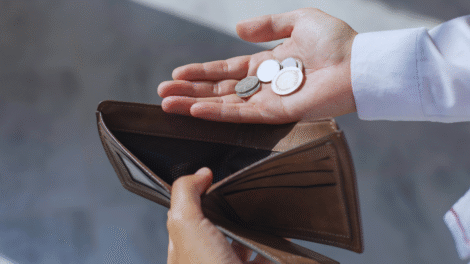 Uma pessoa segura uma carteira marrom quase vazia em uma mão e algumas moedas na outra, destacando o desafio de investir com pouco dinheiro.