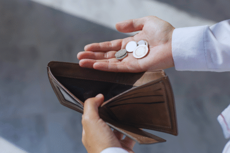 Uma pessoa segura uma carteira marrom quase vazia em uma mão e algumas moedas na outra, destacando o desafio de investir com pouco dinheiro.