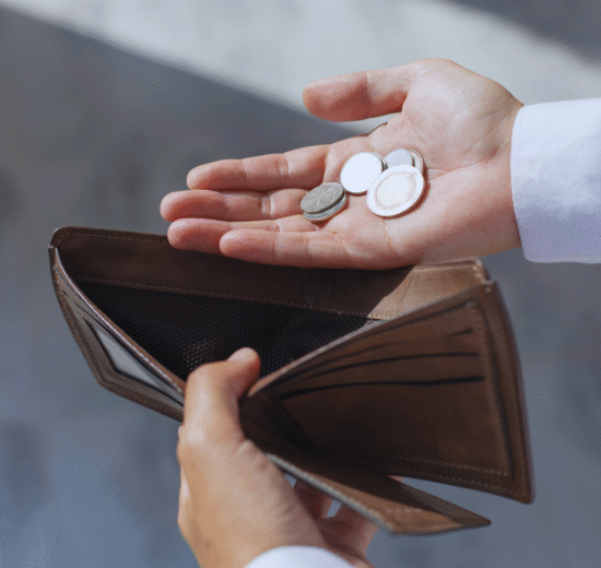 Uma pessoa segura uma carteira marrom quase vazia em uma mão e algumas moedas na outra, destacando o desafio de investir com pouco dinheiro.