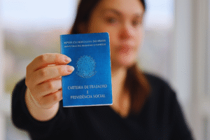 Uma pessoa segura uma Carteira de Trabalho e Previdência Social brasileira em direção à câmera, destacando as recentes melhorias no FGTS para os trabalhadores.