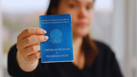 Uma pessoa segura uma Carteira de Trabalho e Previdência Social brasileira em direção à câmera, destacando as recentes melhorias no FGTS para os trabalhadores.
