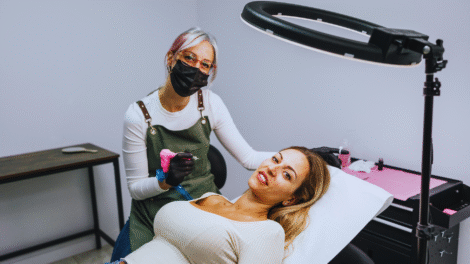 Um micropigmentador usando uma máscara e luvas trabalha em uma tatuagem no braço de uma mulher enquanto ela se deita em uma cadeira no estúdio.