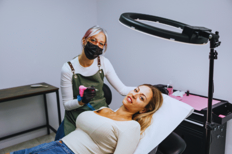 Um micropigmentador usando uma máscara e luvas trabalha em uma tatuagem no braço de uma mulher enquanto ela se deita em uma cadeira no estúdio.
