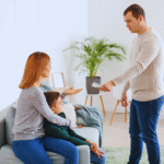 Um homem entrega dinheiro a uma mulher sentada que está com uma criança em uma sala de estar, ilustrando o pagamento da pensão alimentícia retroativa.