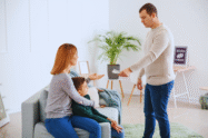 Um homem entrega dinheiro a uma mulher sentada que está com uma criança em uma sala de estar, ilustrando o pagamento da pensão alimentícia retroativa.