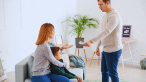 Um homem entrega dinheiro a uma mulher sentada que está com uma criança em uma sala de estar, ilustrando o pagamento da pensão alimentícia retroativa.