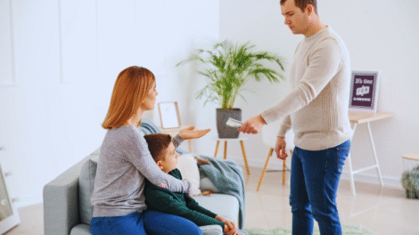 Um homem entrega dinheiro a uma mulher sentada que está com uma criança em uma sala de estar, ilustrando o pagamento da pensão alimentícia retroativa.