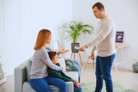 Um homem entrega dinheiro a uma mulher sentada que está com uma criança em uma sala de estar, ilustrando o pagamento da pensão alimentícia retroativa.