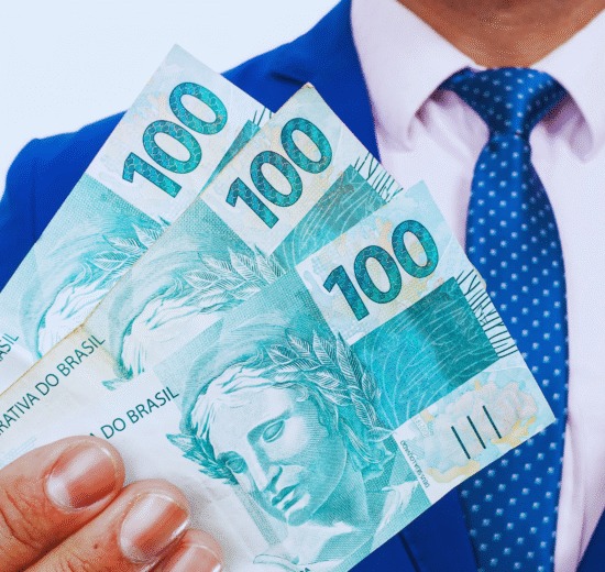 Uma pessoa de terno azul e gravata segura três notas de 100 reais, considerando onde investir 1.000 reais com sabedoria.