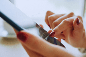 Close-up de uma pessoa com esmalte vermelho usando um smartphone, explorando aplicativos úteis para celular com o dedo indicador na tela.