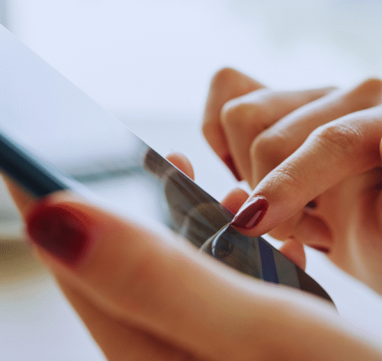 Close-up de uma pessoa com esmalte vermelho usando um smartphone, explorando aplicativos úteis para celular com o dedo indicador na tela.