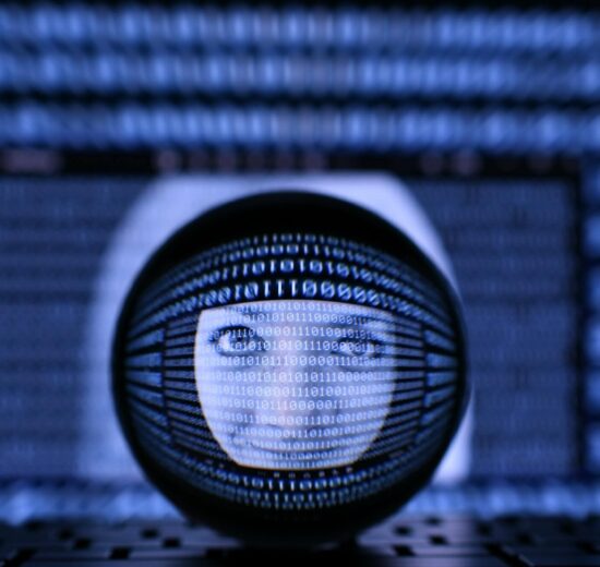 Uma esfera de vidro mostra um rosto digital com código binário sobreposto, refletindo uma tela de computador azulada preenchida com mais números binários ao fundo, simbolizando tecnologia e inteligência artificial.