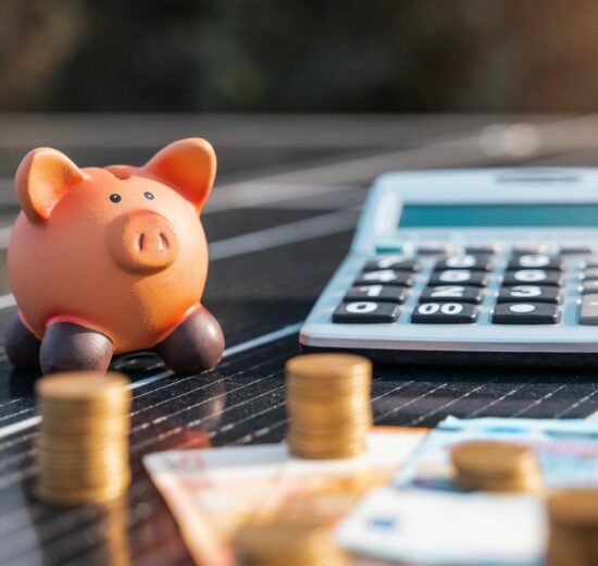 Um cofrinho, uma calculadora, pilhas de moedas e notas são colocados em um painel solar, simbolizando a economia financeira e o investimento em energia renovável.